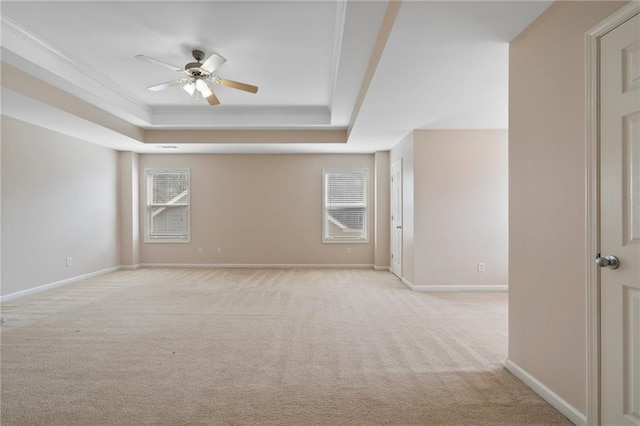 empty room featuring a raised ceiling, light colored carpet, baseboards, and ceiling fan