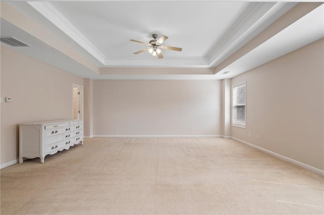 empty room with a raised ceiling, light colored carpet, ceiling fan, and crown molding