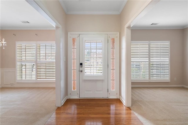 carpeted entrance foyer with visible vents, wood finished floors, and ornamental molding