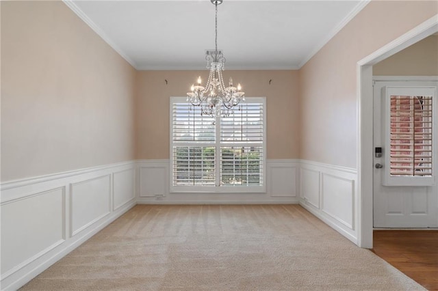 unfurnished dining area with light carpet, wainscoting, an inviting chandelier, and ornamental molding