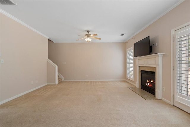 unfurnished living room with visible vents, light colored carpet, a premium fireplace, ornamental molding, and a ceiling fan