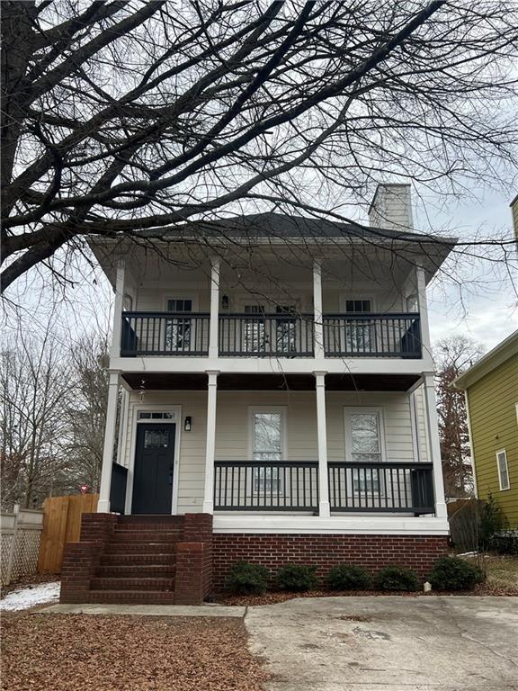 view of front of property featuring a porch, a chimney, fence, and a balcony