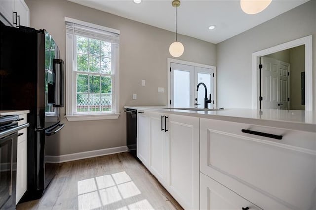 kitchen featuring decorative light fixtures, light wood-style flooring, white cabinetry, a sink, and baseboards