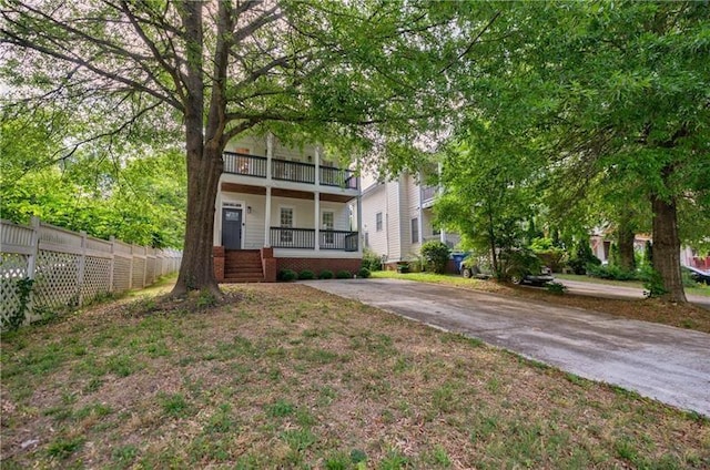 view of front of house featuring a porch, driveway, fence, and a balcony