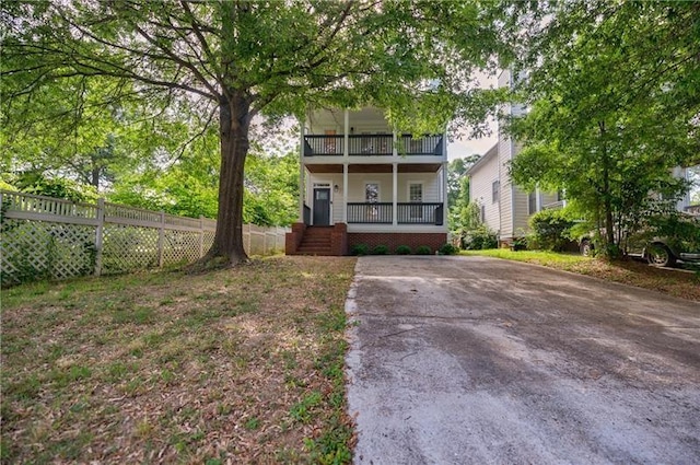 view of front of home with covered porch, fence, and a balcony