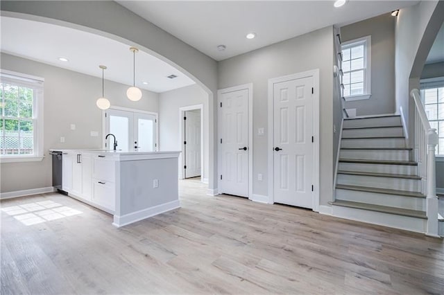 kitchen featuring a healthy amount of sunlight, light wood finished floors, white cabinetry, and arched walkways