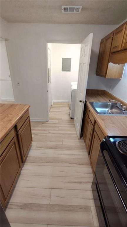 kitchen featuring visible vents, light wood-style flooring, a sink, washer / dryer, and black range with electric cooktop