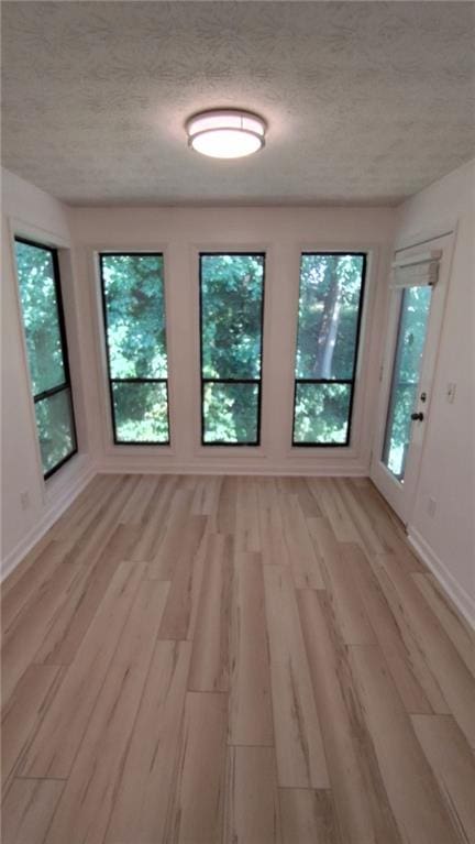 empty room with light wood-type flooring, baseboards, and a textured ceiling