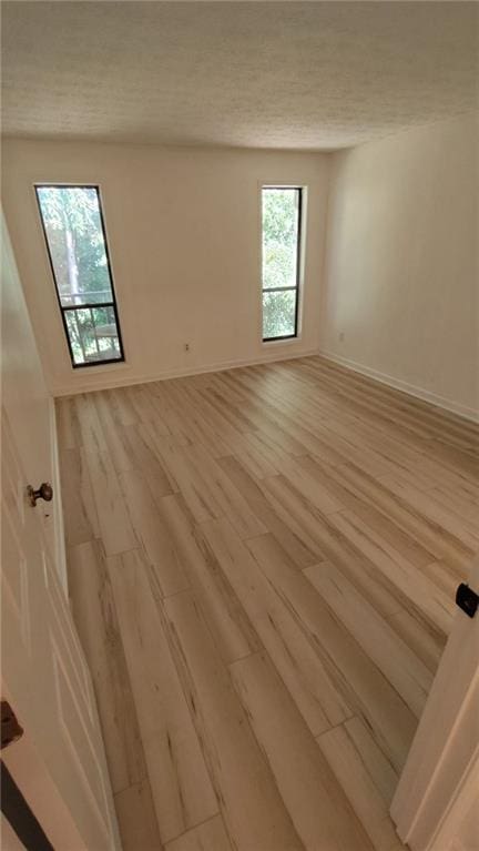 unfurnished room featuring light wood-type flooring, a textured ceiling, and baseboards