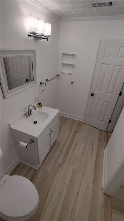 bathroom with toilet, vanity, wood finished floors, crown molding, and a textured ceiling