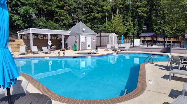 pool featuring a hot tub, a patio, an outbuilding, fence, and a shed