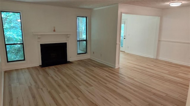 unfurnished living room featuring a fireplace with flush hearth, plenty of natural light, and light wood finished floors