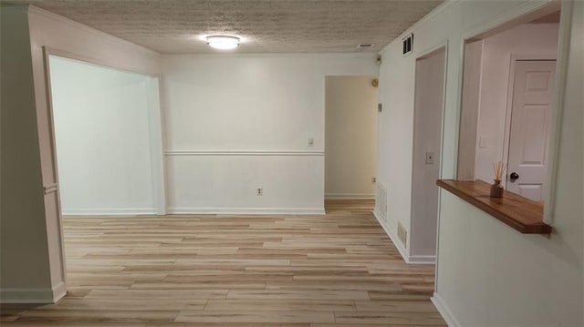 empty room featuring light wood-type flooring, baseboards, visible vents, and a textured ceiling