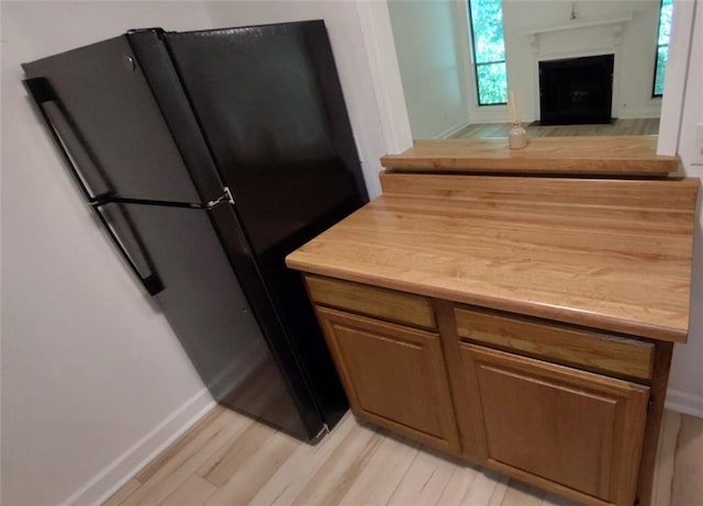 kitchen featuring brown cabinets, light countertops, light wood-style floors, freestanding refrigerator, and a fireplace with flush hearth