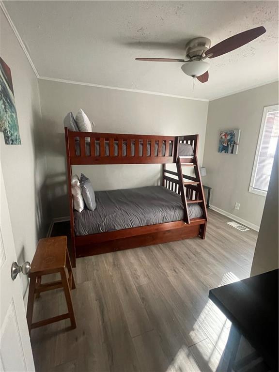 bedroom with wood-type flooring, ceiling fan, and ornamental molding