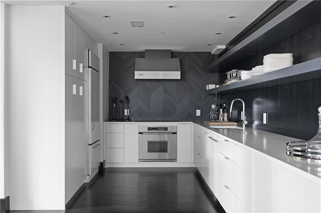 kitchen with white cabinetry, sink, stainless steel oven, and wall chimney exhaust hood