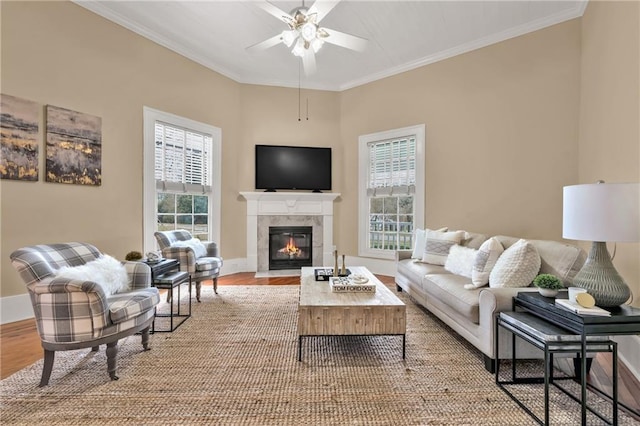 living room featuring ceiling fan, a fireplace with flush hearth, baseboards, light wood-type flooring, and crown molding