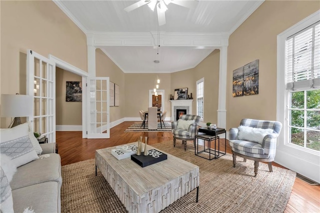 living area with crown molding, ceiling fan, wood finished floors, a warm lit fireplace, and baseboards