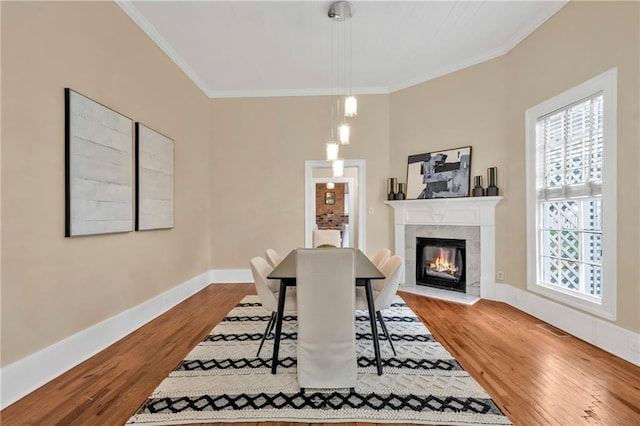 dining space with ornamental molding, a tiled fireplace, wood finished floors, and baseboards