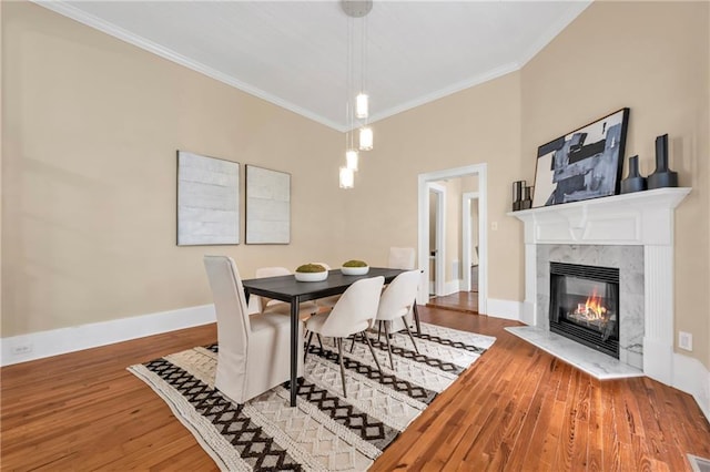 dining room with a high end fireplace, crown molding, baseboards, and wood finished floors