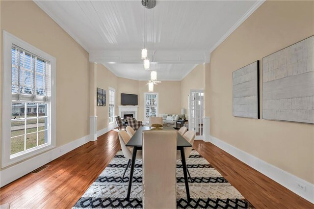 dining space with crown molding, a fireplace, baseboards, and wood finished floors