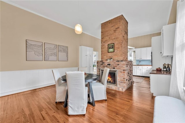 dining room featuring light wood-type flooring, ornamental molding, a fireplace, and wainscoting