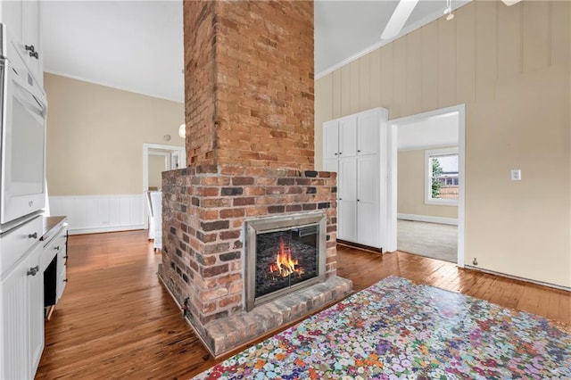 living room featuring wood-type flooring, a fireplace, ornamental molding, and vaulted ceiling