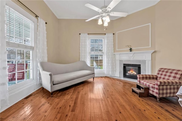 sitting room with wood-type flooring, visible vents, a fireplace, and ceiling fan