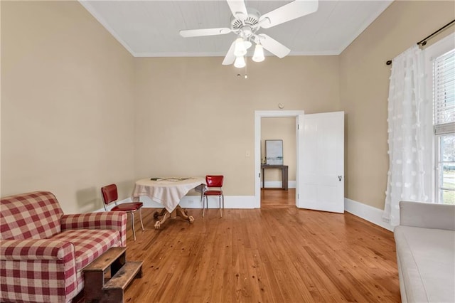 living area with a ceiling fan, crown molding, baseboards, and wood finished floors