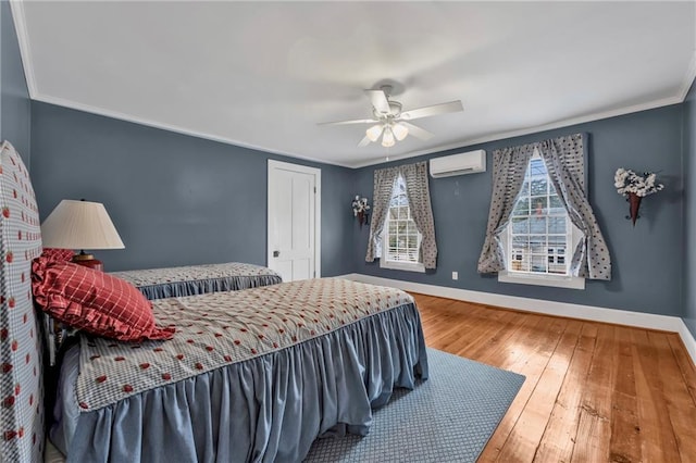 bedroom with a wall unit AC, wood-type flooring, baseboards, and crown molding