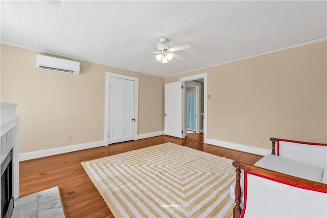 unfurnished bedroom featuring ceiling fan, a wall unit AC, wood finished floors, a fireplace with flush hearth, and baseboards