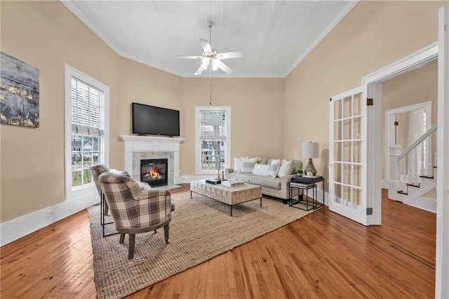 living room with crown molding, a glass covered fireplace, ceiling fan, baseboards, and hardwood / wood-style flooring