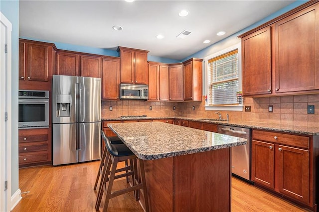 kitchen featuring sink, light hardwood / wood-style flooring, backsplash, appliances with stainless steel finishes, and a center island