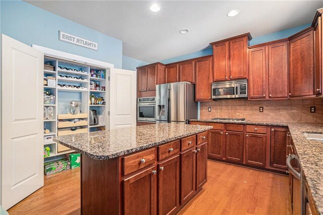 kitchen featuring light stone counters, a center island, stainless steel appliances, light hardwood / wood-style flooring, and backsplash