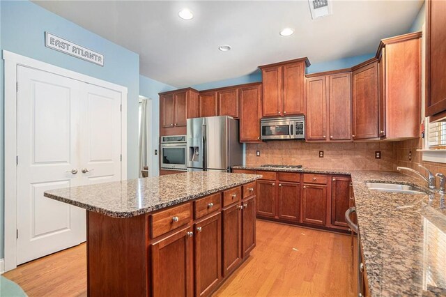 kitchen with light stone counters, sink, a kitchen island, light hardwood / wood-style flooring, and stainless steel appliances