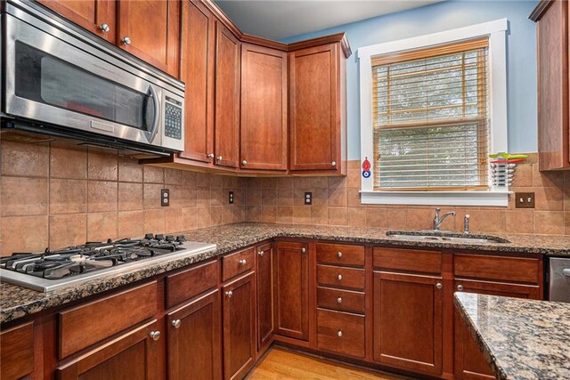 kitchen featuring light wood-type flooring, dark stone countertops, sink, and stainless steel appliances