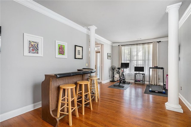 exercise room with ornate columns, ornamental molding, bar, and dark wood-type flooring