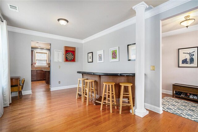 bar featuring ornamental molding, light hardwood / wood-style flooring, and decorative columns