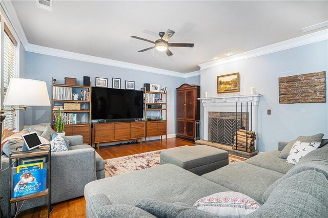 living room featuring wood-type flooring, a fireplace, crown molding, and ceiling fan