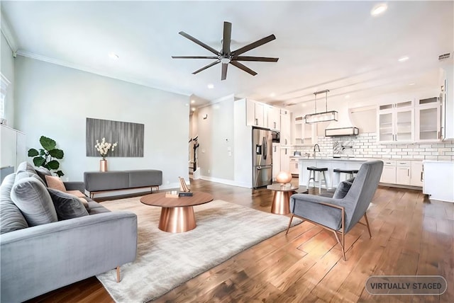 living room with ceiling fan, sink, ornamental molding, and dark wood-type flooring