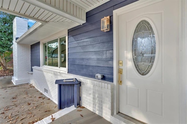 doorway to property featuring crawl space, a chimney, and brick siding