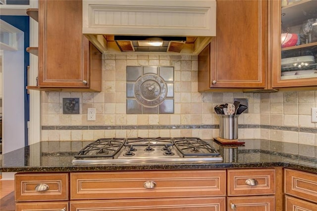 kitchen featuring stainless steel gas stovetop, backsplash, glass insert cabinets, and brown cabinetry