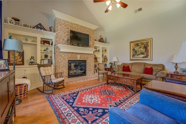 living room featuring a ceiling fan, light wood-style floors, a brick fireplace, and high vaulted ceiling