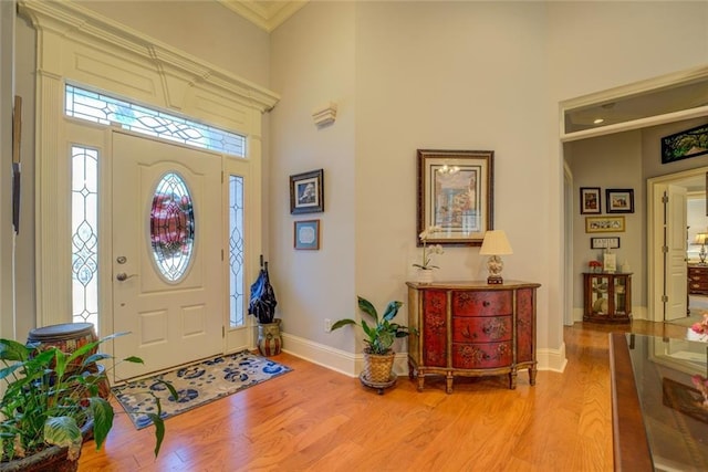 foyer entrance with light wood-style floors, a high ceiling, baseboards, plenty of natural light, and ornamental molding
