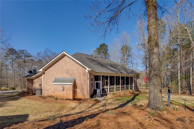 view of home's exterior featuring a sunroom, brick siding, a yard, and central AC unit