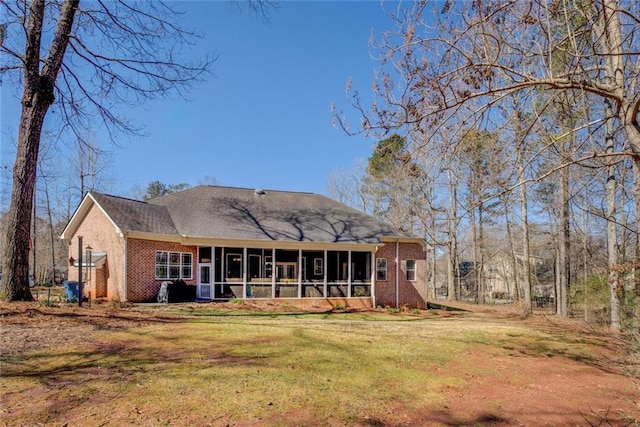 back of property featuring a sunroom, brick siding, and a lawn
