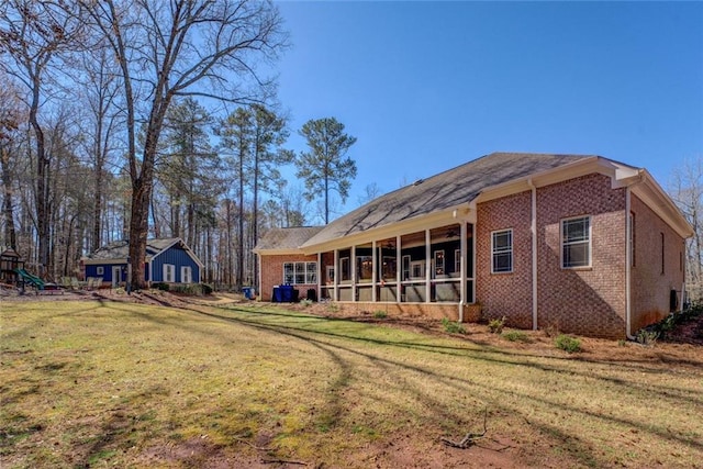 rear view of property with brick siding, a sunroom, a lawn, and a playground