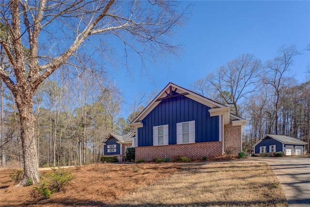 view of front of house with board and batten siding, a detached garage, brick siding, and an outbuilding
