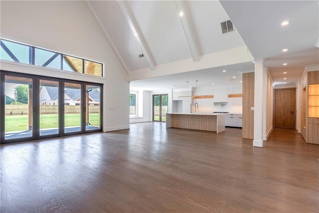 unfurnished living room with beam ceiling, dark hardwood / wood-style flooring, sink, and high vaulted ceiling