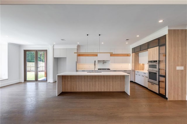 kitchen featuring sink, crown molding, hardwood / wood-style floors, a center island with sink, and white cabinets